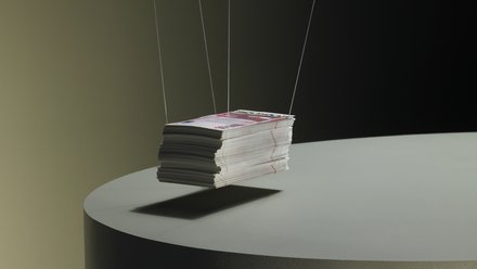 Ein Stapel Printmagazine, an dünnen Fäden aufgehängt, schwebt knapp über einem runden Podest; dunkler Studiohintergrund und weiches Seitenlicht.