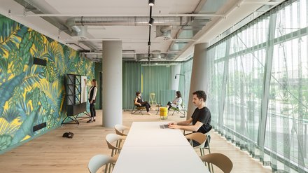 Langer Raum mit Arbeitsplätzen, Sitzbänken und Blick nach außen.