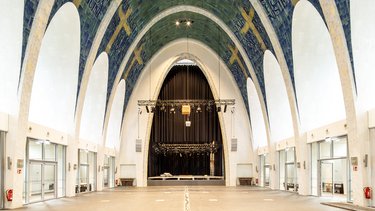 Großer Kirchenraum mit hohen Gewölben, Fliesenmosaik und einer Bühne im Hintergrund.