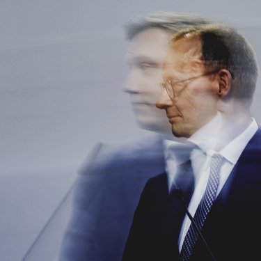 Pressefoto eines Politikers am Rednerpult, Seitenansicht mit Bewegungsunschärfe vor neutralem Hintergrund.