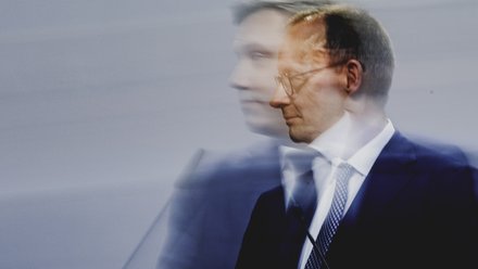 Pressefoto eines Politikers am Rednerpult, Seitenansicht mit Bewegungsunschärfe vor neutralem Hintergrund.