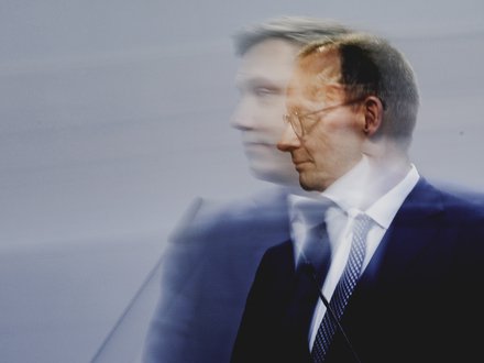 Pressefoto eines Politikers am Rednerpult, Seitenansicht mit Bewegungsunschärfe vor neutralem Hintergrund.