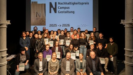 Gruppenfoto auf Bühne: rund 40 Personen mit Urkunden vor Leinwand „Nachhaltigkeitspreis Campus Gestaltung 2025–2026“.