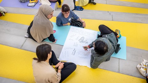 Gruppe diskutiert Ideen auf einer beschrifteten Papierfläche im Hörsaal.
