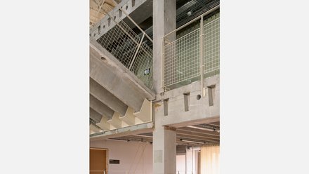 Detailaufnahme einer Etage mit massiven Pfeilern und Deckenbalken sowie einem hellen Gittergeländer. 