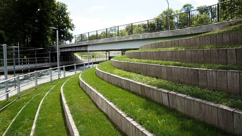 Terrassenförmige Sitzstufen aus Beton mit Grasflächen neben einem Kanal und einer Brücke.