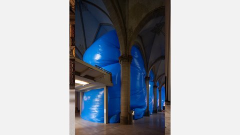 Kirchenraum mit hohen Gewölben und einer großformatigen blauen Stoffinstallation, die sich zwischen den Säulen ausbreitet.