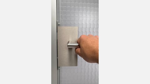 Hand greift einen rechteckigen, gebürsteten Metall-Türgriff vor einer weiß-gemusterten Wand