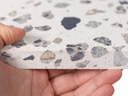 Hand hält eine Platte mit Terrazzo-Muster aus verschieden großen Steinfragmenten