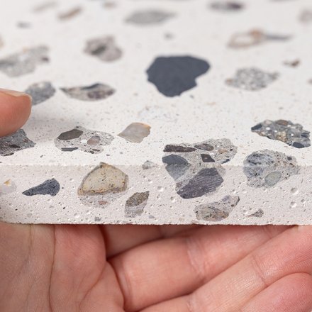 Hand hält eine Platte mit Terrazzo-Muster aus verschieden großen Steinfragmenten
