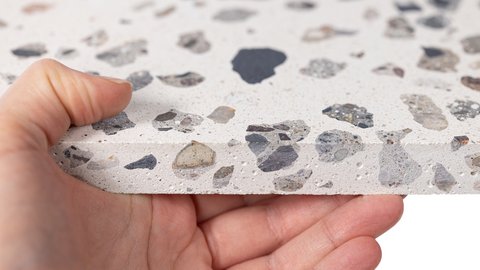 Hand hält eine Platte mit Terrazzo-Muster aus verschieden großen Steinfragmenten