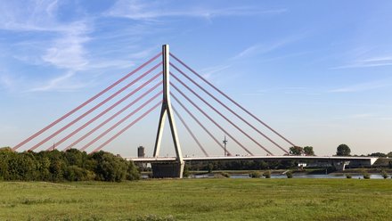 Im Vordergrund ist eine grüne Wiese zu sehen. Im Hintergrund ist die Niederrhein-Brücke in Wesel abgebildet. 