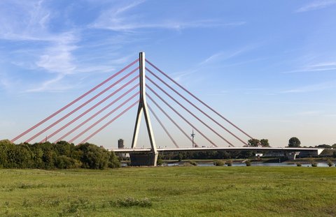 Im Vordergrund ist eine grüne Wiese zu sehen. Im Hintergrund ist die Niederrhein-Brücke in Wesel abgebildet. 