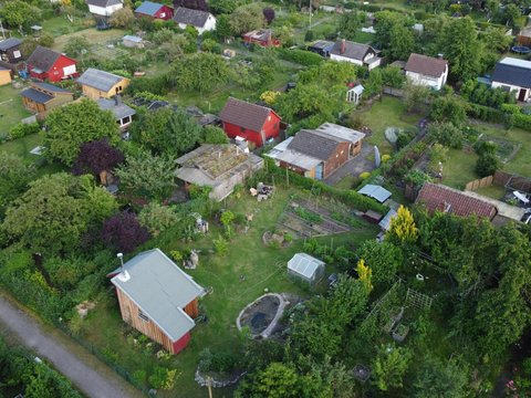 Luftaufnahme einer Kleingartenanlage mit kleinen Gartenhäusern, Beeten und vielen Bäumen.