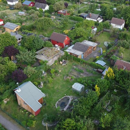 Luftaufnahme einer Kleingartenanlage mit kleinen Gartenhäusern, Beeten und vielen Bäumen.
