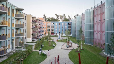 Grüner Innenhof mit Spielgeräten, umgeben von mehrgeschossigen Wohnhäusern.