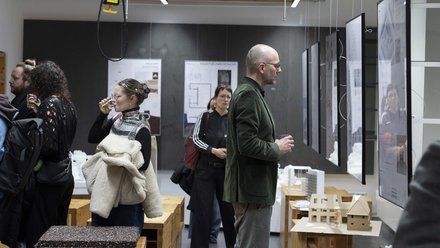 Gäste betrachten aufgehängte Plakate und Architekturmodelle in einer Ausstellung im Studio.