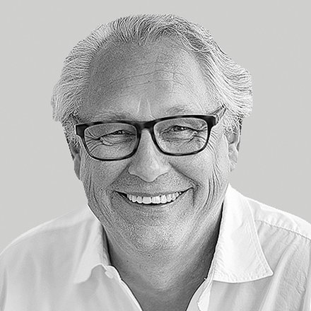 Schwarzweiß-Nahaufnahme: lächelnder Mann mit Brille und weißem Hemd vor neutral grauem Hintergrund.