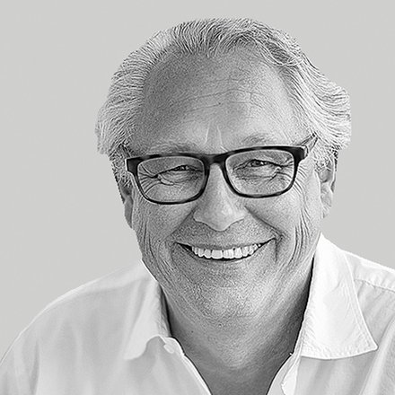 Schwarzweiß-Nahaufnahme: lächelnder Mann mit Brille und weißem Hemd vor neutral grauem Hintergrund.