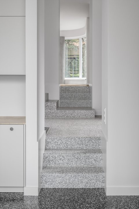 Heller Innenraum mit gestufter Terrazzotreppe, großen Fenstern und klar gegliederten weißen Wänden.