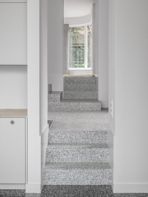 Heller Innenraum mit gestufter Terrazzotreppe, großen Fenstern und klar gegliederten weißen Wänden.