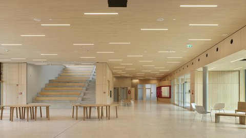 Heller, großzügiger Foyerbereich mit breiter Treppe, Holzvertäfelungen, mehreren Tischen und Stühlen sowie großen Fenstern