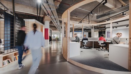 Offener Coworking-Bereich mit runder Holzstruktur, Arbeitsplätzen und Menschen beim Arbeiten.