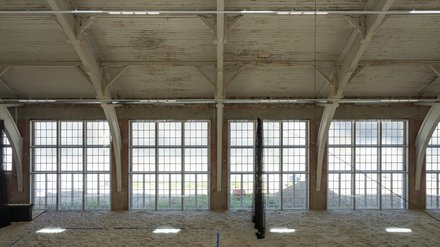 Große, helle Halle mit hohen Fenstern und Sandboden