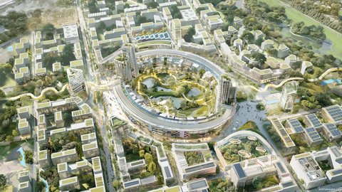 Luftbild eines städtischen Areals, das sich um ein zentrales, großes, kreisförmiges Gebäude mit einem begrünten Innenhof anordnet. In diesem Innenhof befinden sich Teiche und Gehwege. Zwei Hochhäuser flankieren den ringförmigen Komplex. Die umliegende Bebauung besteht aus modernen Büround Wohngebäuden mit Gründächern und Solaranlagen, die durch geschwungene Fußgängerwege und Grünstreifen miteinander verbunden sind.