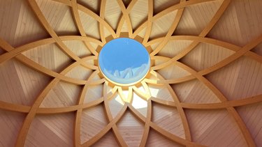 Blick nach oben auf eine kunstvoll gefügte Holzkuppel mit zentralem Oberlicht.