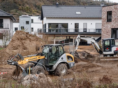 Baustelle mit Radlader, Minibagger und Erdhügel vor modernen Einfamilienhäusern.