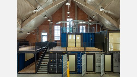 Innenraum einer umgebauten Industriehalle mit Containern und Treppe