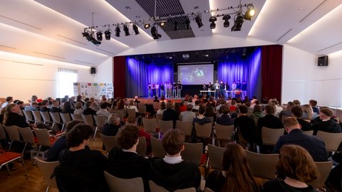 Präsentationsveranstaltung von „Architektur macht Schule“ mit Schülerinnen und Schülern auf einer Bühne vor einem großen Publikum.