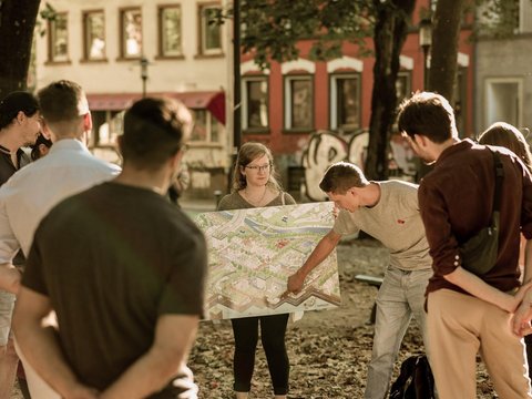 Gruppe von Menschen betrachtet gemeinsam einen großen Stadtplan im öffentlichen Raum von Saarbrücken.