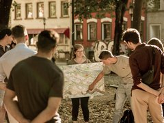 Gruppe von Menschen betrachtet gemeinsam einen großen Stadtplan im öffentlichen Raum von Saarbrücken.