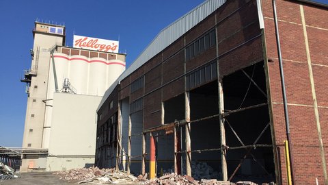 Fabrikhalle mit rausgebrochenen Fenstern und Schutt auf dem Boden. Im Hintergrund ein weißer Turm mit einem Kellogs Schild 