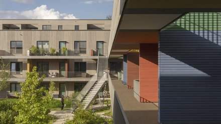 Farbenfrohe Fassaden und Balkone einer modernen Wohnanlage, mit einer Person auf der Terrasse.