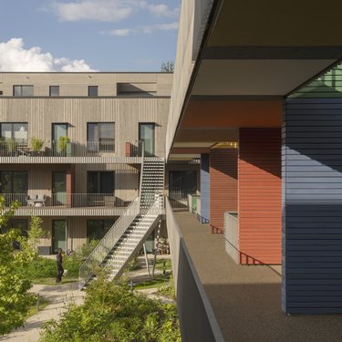 Farbenfrohe Fassaden und Balkone einer modernen Wohnanlage, mit einer Person auf der Terrasse.