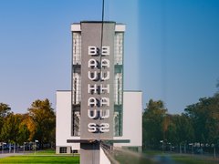 Fassade des weißen Bauhaus-Gebäudes mit vertikal angeordneten Buchstaben "BAUHAUS" und "WEIMAR" vor blauem Himmel und Bäumen.