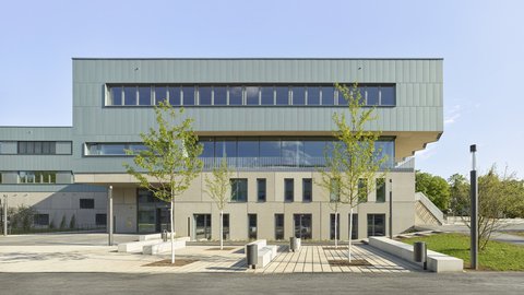 Moderner mehrstöckiger Gebäudekomplex mit großen Fenstern und drei jungen Bäumen im Vordergrund