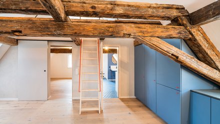 Innenraum mit Holzbalken und Leiter in der Mitte des Raumes.