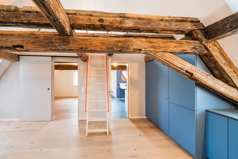 Innenraum mit Holzbalken und Leiter in der Mitte des Raumes.
