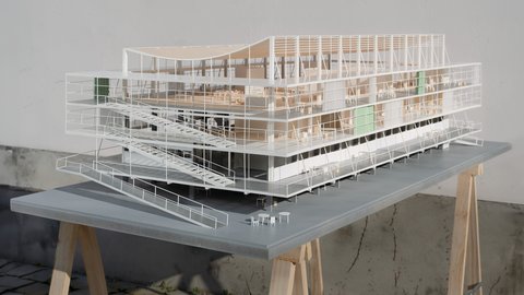Architekturmodell eines mehrgeschossigen Gebäudes mit transparenter Gebäudehülle, außenliegenden Rampen und geschwungenem Dach.
