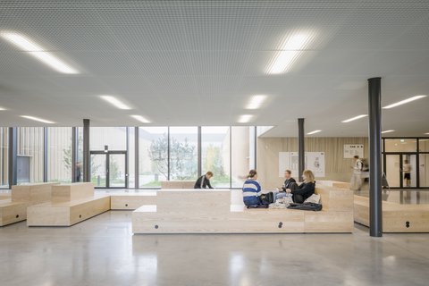 Offener Aufenthaltsbereich mit Sitzstufen, großen Fenstern und flexiblen Lernplätzen.
