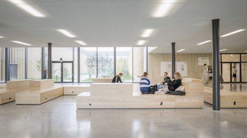Offener Aufenthaltsbereich mit Sitzstufen, großen Fenstern und flexiblen Lernplätzen.