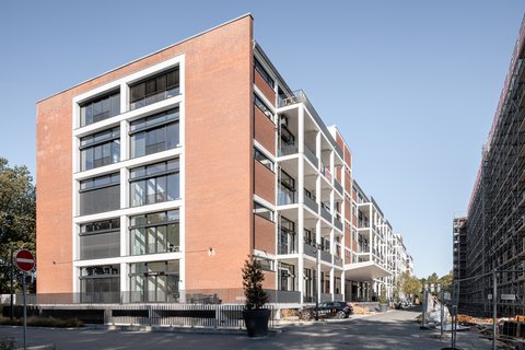 Mehrstöckiges Gebäude mit roter Backsteinfassade und großen Fenstern an einer Straße mit parkenden Autos