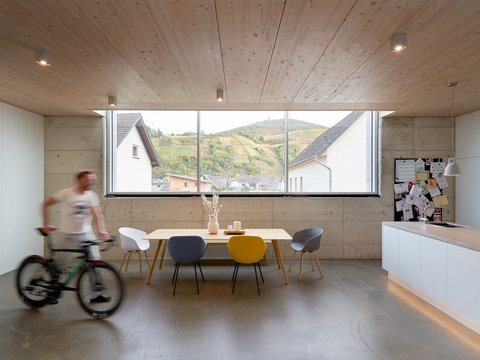 Heller, offener Essbereich mit Holzdecke und großem Panoramafenster mit Blick auf Weinberge; im Vordergrund ein vorbeifahrender, unscharfer Radfahrer.