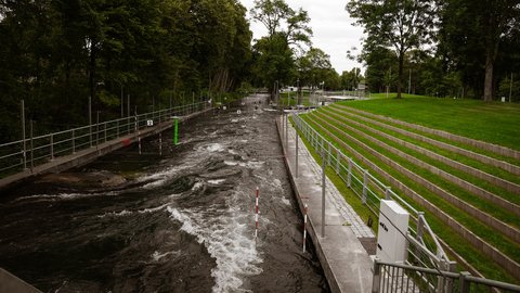 Wildwasserkanal mit begrünten Sitzstufen und Bäumen entlang des Ufers.