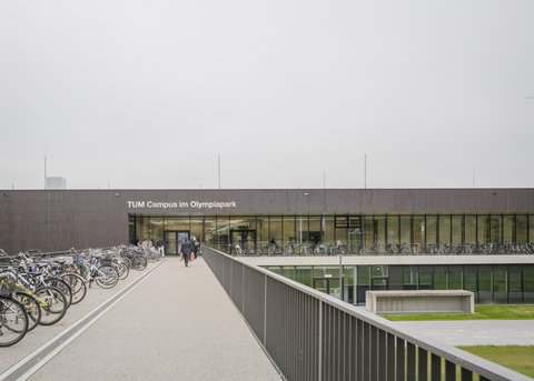 Campusgebäude mit Fahrradstellplätzen und Zugang über eine erhöhte Promenade.