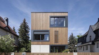 Modernes Einfamilienhaus mit klarer Kubusform, Holzfassade und großen Fensteröffnungen.